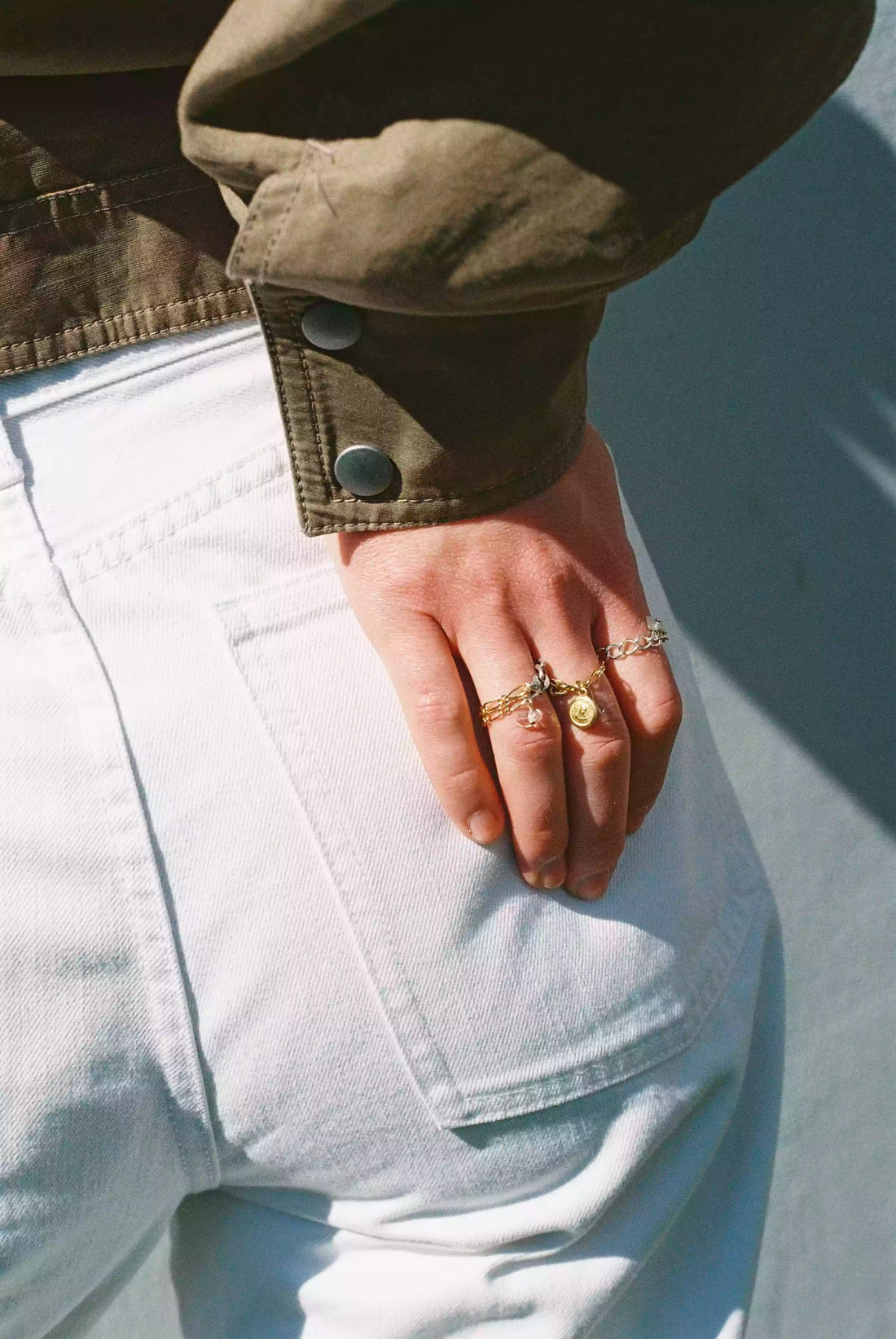 Le modèle pose sa main sur son fessier, on voit qu'il porte trois bagues upcyclées uniques Tête d'Orange de la nouvelle collection, qui scintillent au soleil.