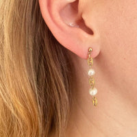 La modèle porte une des boucles d'oreille à composer. Celle-ci est une boucle pendante avec une alternance d'un grain de café plaqué or et une perle d'eau douce vintage, repetée trois fois.