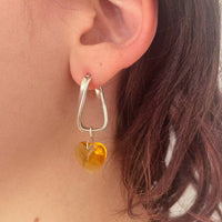 La modèle porte la deuxième boucle d'oreille faite main Tête d'Orange. Une créole torsadée en argent, avec un cœur en cristal orange suspendu.
