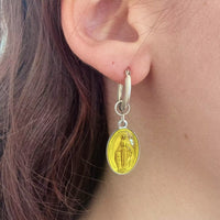 Une des boucle d'oreille portée. C'est celle avec la créole en argent et une médaille jaune suspendue. On voit les détails de ce médaillon, une religieuse debout.