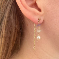 Gros plan sur une oreille avec une des boucle portée. A l'avant, une perle d'eau douce et deux pierres semi-précieuses, et accrochée au fermoir de la boucle, une chaîne plaquée or vintage.
