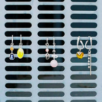 Trois paires de boucles d'oreilles de la nouvelle collection de bijoux Tête d'Orange, dont la paire en argent avec le cœur en cristal orange, tout à droite.