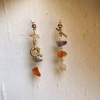 Photo des deux boucles d'oreilles uniques sur un fond blanc texturé. Elles forment un ensemble très coloré et original.