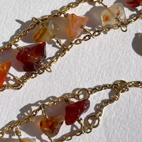 Photo en gros plan des détails d'assemblage de ce collier, qui a été réalisé à la main à Strasbourg. On voit la variété de formes et de couleurs des cornalines, qui sont plus ou moins orangées, rouges, blanches. Elles sont accrochées aux chaînes par des tiges plaquées or mises en queue de cochon.