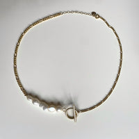 Ce collier upcyclé, réalisé avec des chaînes vintages plaquées or et des perles d'eau douce.