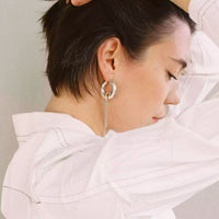 Une modèle porte la deuxième pièce de la paire. C'est la boucles d'oreille la plus longue.