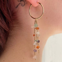 Photo portée d'une boucle d'oreille de cette paire symétrique. On voit les trois chaînes plaquées or vintage auxquelles sont accrochées des pierres semi-précieuses multicolores.