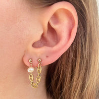 Boucles d'oreilles photographiée portée sur notre modèle. Elle se porte sur deux trous du lobe, et est composée d'une perle d'eau douce suivie d'un morceau de chaîne grain de café plaquée or vintage.