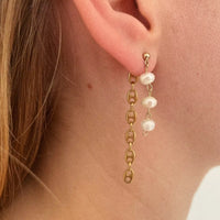 Photo portée d'une des boucles d'oreilles. A l'avant, la boucle est composée de trois perles d'eau douce pendantes, et accrochée au fermoir, un bout de chaîne vintage grain de café plaquée or.