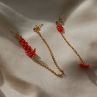 Boucles d'oreilles upcyclées ornées de coraux rouges posées sur un tissu clair.