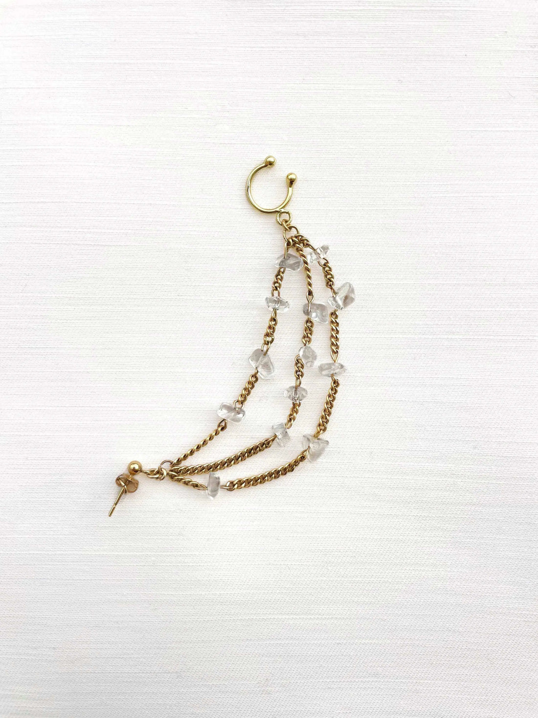 Cette mono boucle associe 3 chaînes plaquées or parsemées chacune de pierres semi-précieuses transparentes.