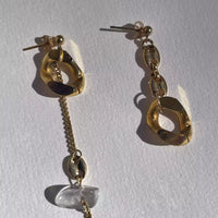 Gros plan de la paire de boucle d'oreille sur fond blanc. Le plaqué or reflète la lumière, l'asymétrie rend ce bijou original.