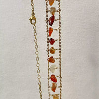 Photo du collier suspendu à la verticale, sur fond blanc. On voit la quinzaine de cornaline qui composent le collier, qui a une structure qui pourrait s'apparenter à une échelle.