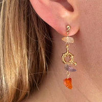 La modèle porte sur son oreille la première boucle. Elle est très colorée. Il y a, de bas en haut, une cornaline, une améthyste, un fermoir décoratif plaqué or, et une cornaline pâle en haut.