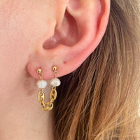Photo portée d'une boucle d'oreille upcyclée. Celle-ci s'attache sur deux trous du lobe. Une chaîne vintage grain de café fait le lien entre les deux trous, et aux extrémités, deux perles d'eau douce chinées à Strasbourg.