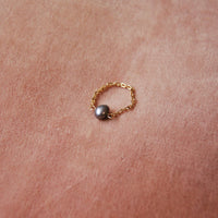 Bague upcyclée ornée d'une perle d'eau douce noire posée sur un fond rose.