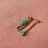 Boucles d'oreilles upcyclées ornées de quartz verts posées sur un tissu rose.