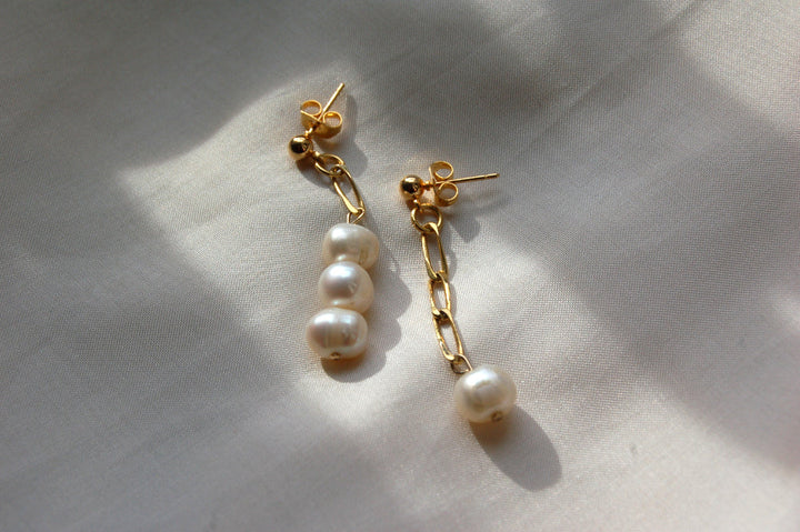 Boucles d'oreilles en plaqué or ornées de perles d'eau douce posées sur un tissu blanc. 