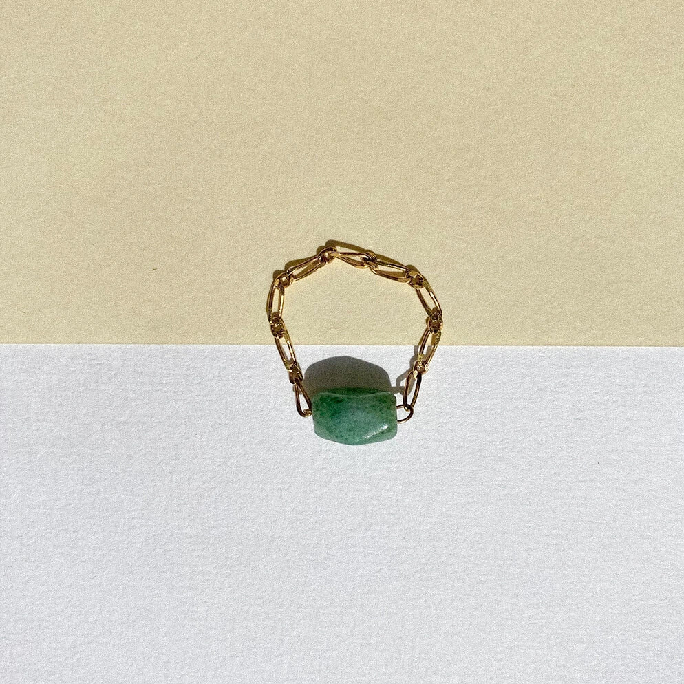 Bague upcyclée ornée d'un quartz vert posée sur un fond bicolore.