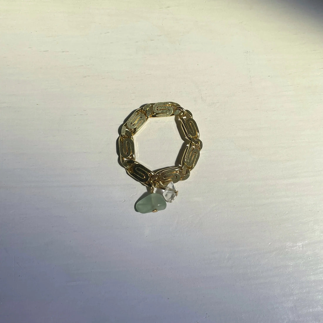 La bague faite main est posée sur fond blanc, on voit bien la maille palmier et les deux petites pierres vertes et transparentes 