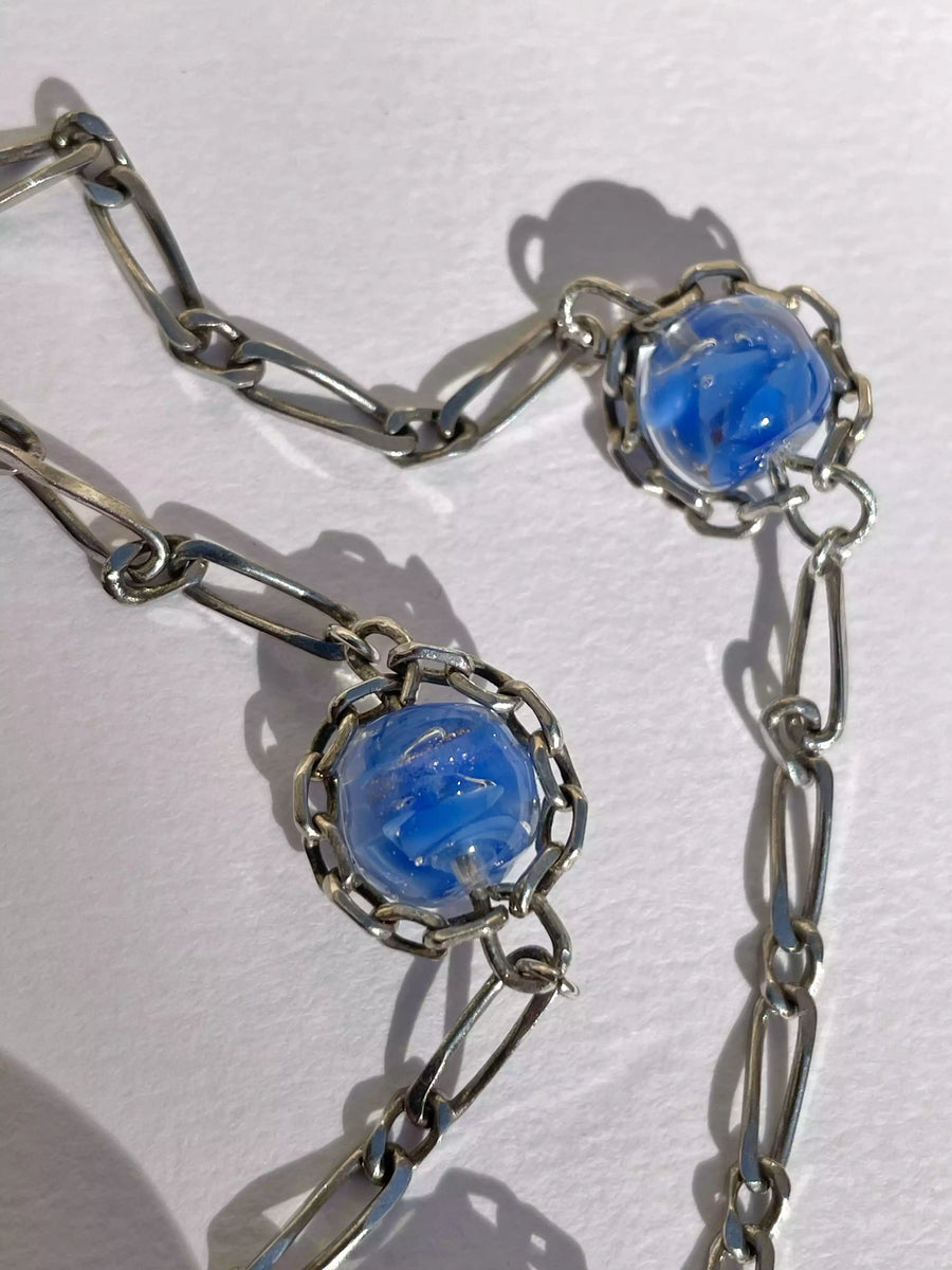 Zoom sur le collier, et notamment les verres de murano entourée de chaînes en argent, qui forment un motif aux allures de soleil. On voit le travail fait main à Strasbourg sur ce collier.