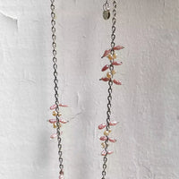 Photo du collier suspendu devant un fond blanc texturé. On voit l'alternance des motifs formés par l'assemblage des perles d'eau douce sur la chaîne en argent.