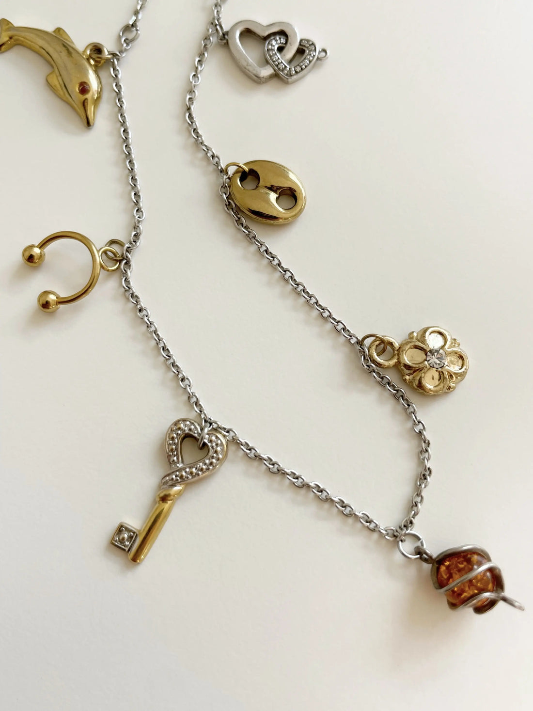 Photo rapprochée du collier pour voir en détail tous les pendentifs. Il y a un dauphin, un piercing, une clé, etc.