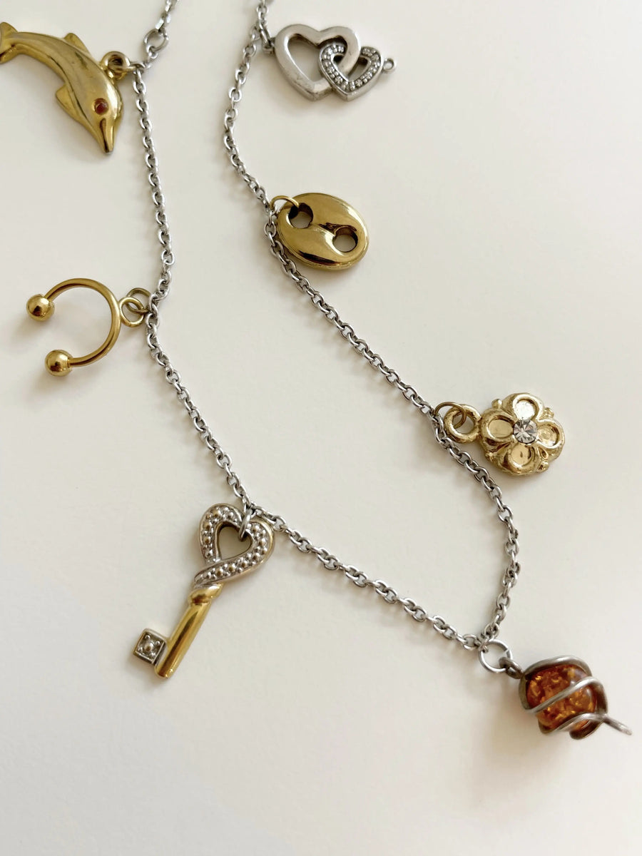 Photo rapprochée du collier pour voir en détail tous les pendentifs. Il y a un dauphin, un piercing, une clé, etc.