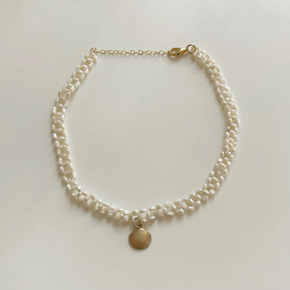 Le collier fait en perles d'eau douces vintages est posé sur un fond blanc. Il est orné d'un pendentif plaqué or en forme de coquillage en son centre.