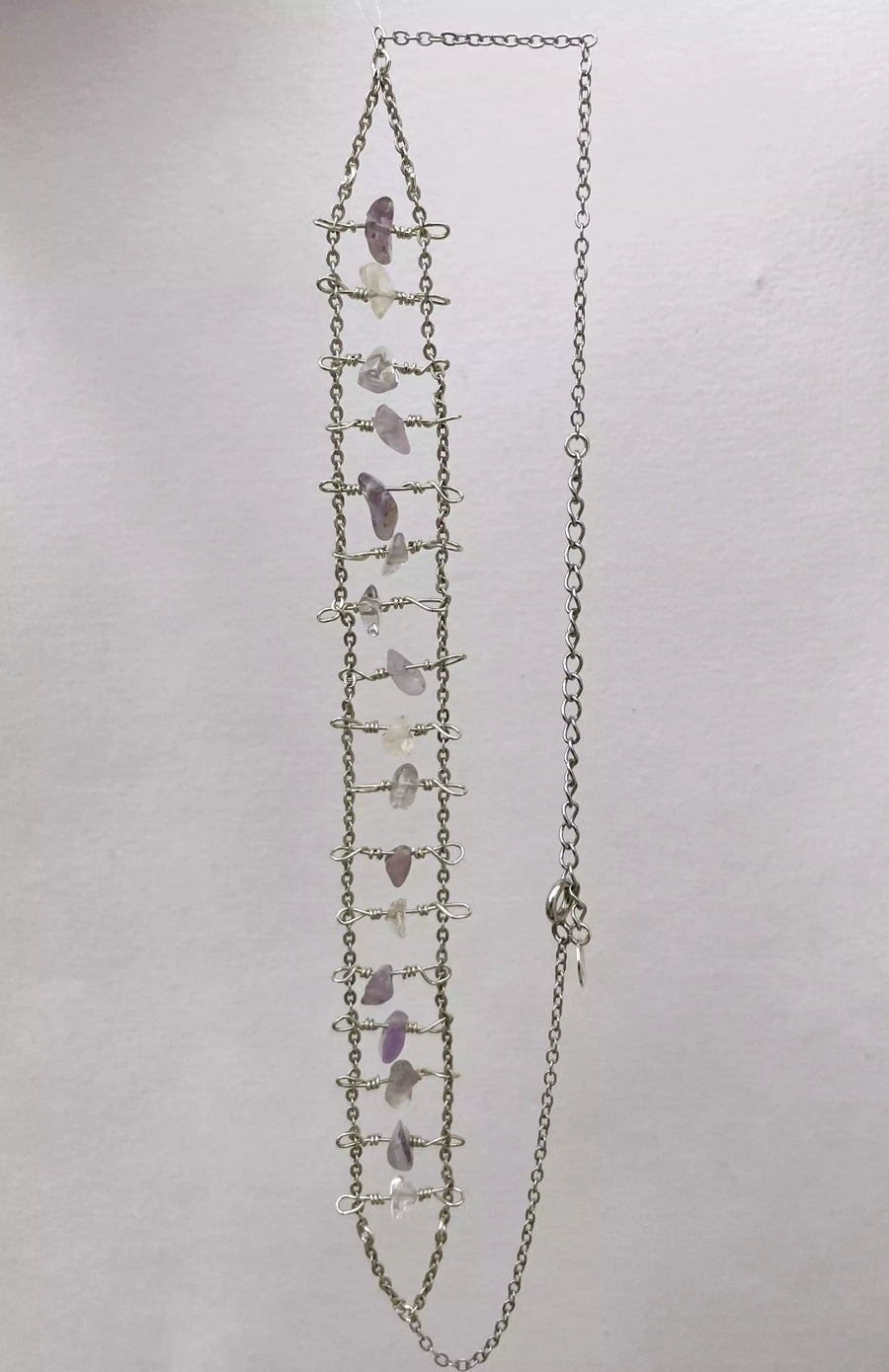 Photo du collier unique fait main sur fond blanc. On le voit en entier, à la verticale. Ce collier pourrait ressembler à la structure d'une échelle.