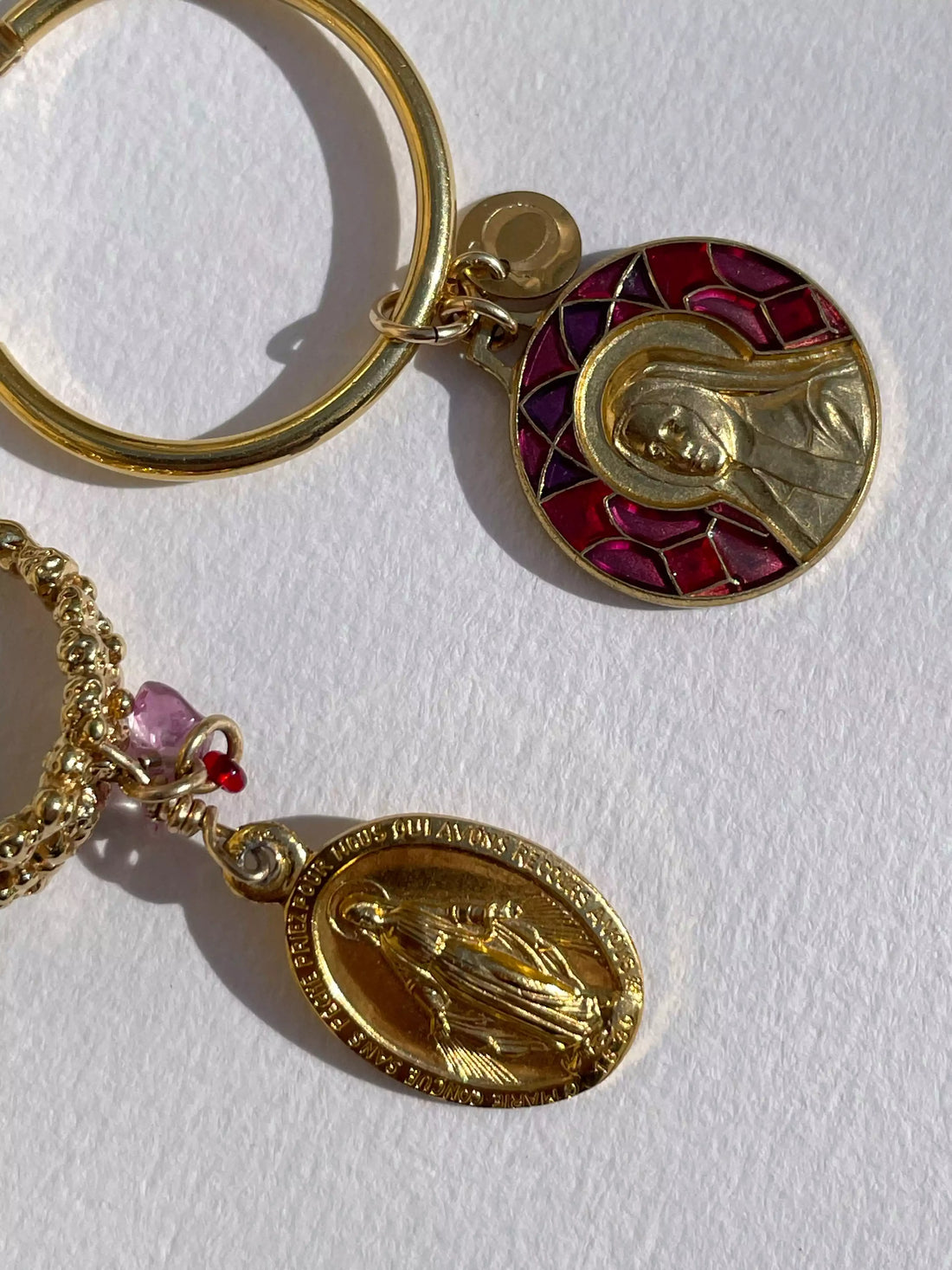Gros plan des détails des médaillons qui sont suspendus aux créoles. L'un est un médaillon religieux avec un motif de vitrail rouge, et l'autre est un médaillon avec une religieuse debout entièrement plaqué or.