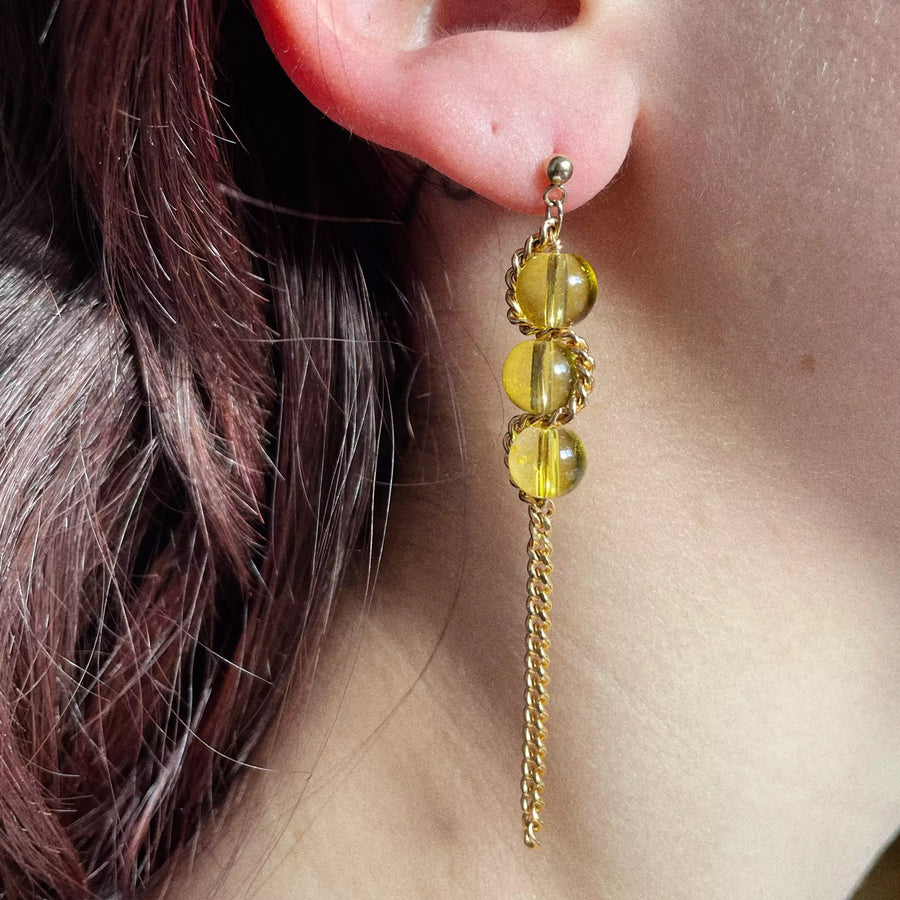 Le modèle porte une des boucles d'oreilles, c'est celle avec trois perles jaunes et une chaîne vintage plaquée or qui s'entrelace sur les trois perles avant de retomber sur le reste de la boucle pour faire une pièce pendante