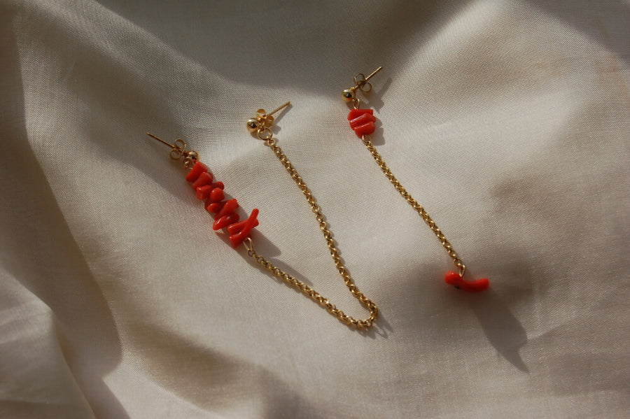 Boucles d'oreilles upcyclées ornées de coraux rouges posées sur un tissu clair. 