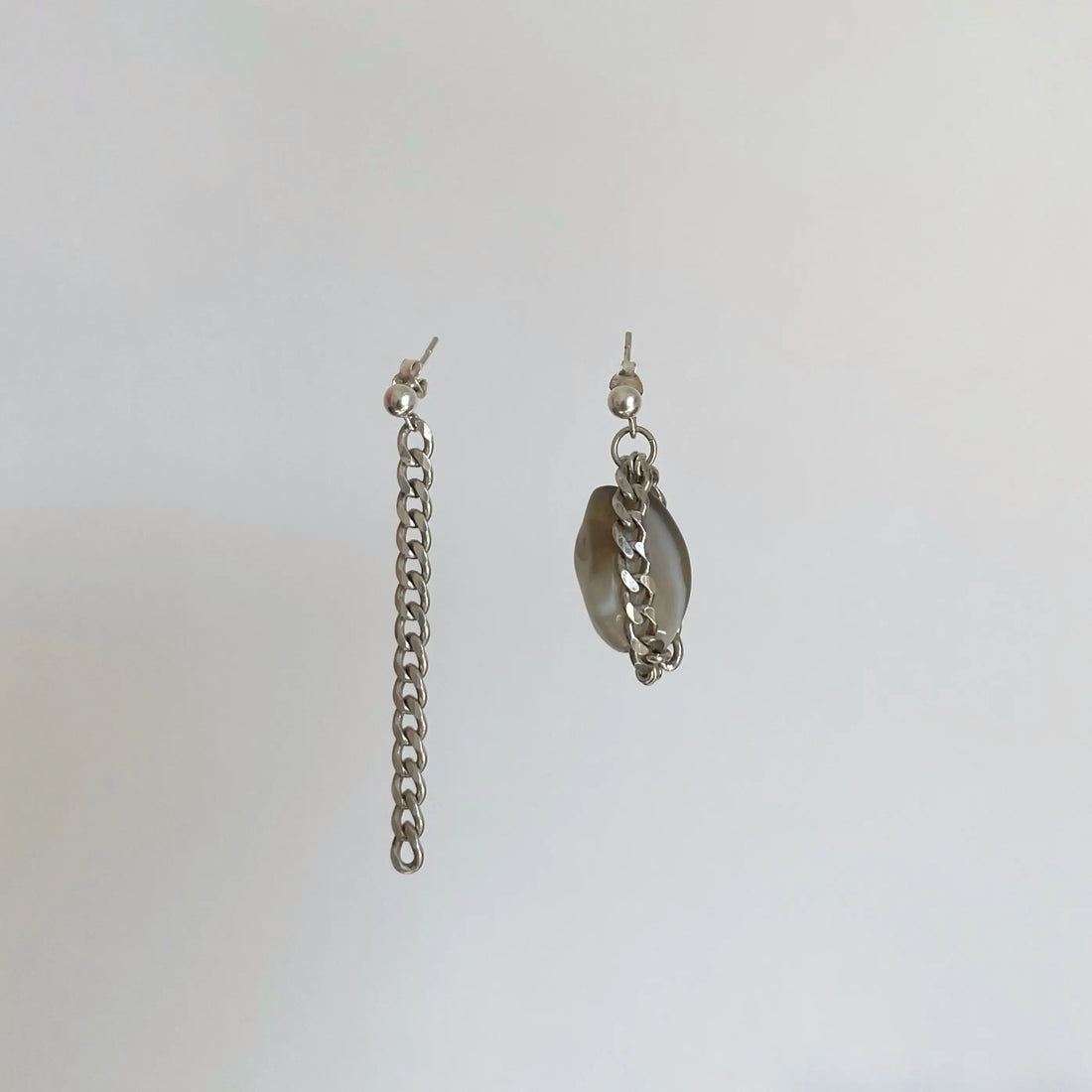 Les boucles d'oreilles upcyclées tout en argent sur fond blanc. On voit l'asymétrie de longueur très tendance.