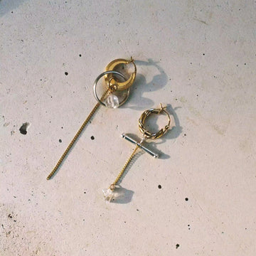 La paire de boucle d'oreille déposée sur un fond de béton texturé. Boucles d'oreilles asymétriques avec un mélange de plaqué or et d'argent.