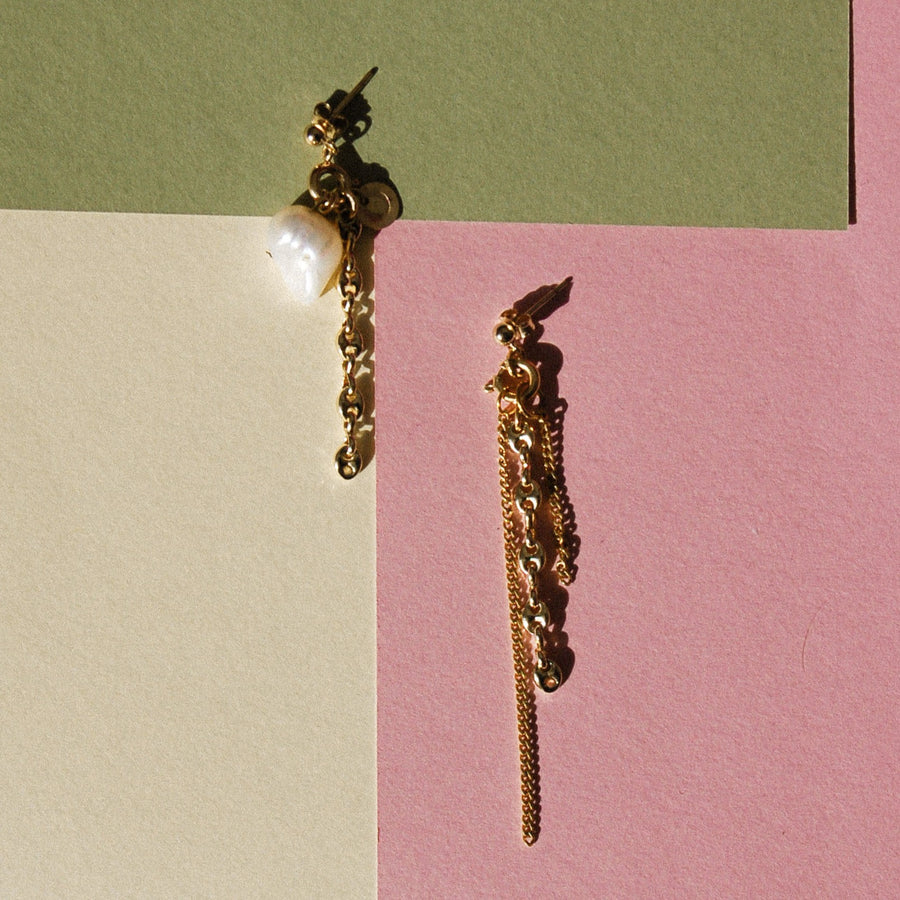 Boucles d'oreilles upcyclées ornées de chaînes et d'une grosse perle d'eau douce posées sur un fond coloré tricolore. 