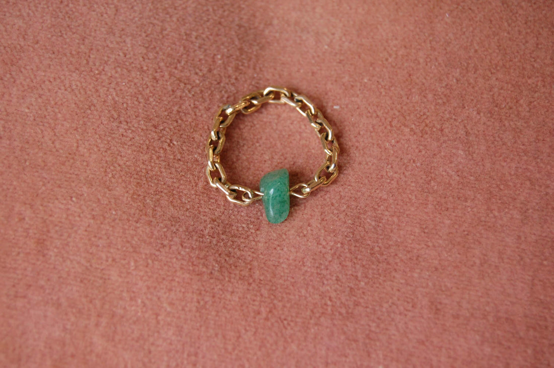 Bague upcyclée ornée d'un quartz vert posée sur un fond vert