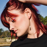 Femme de profil aux cheveux bordeaux - rouges portant une paire de boucles d'oreilles pendantes constitué d'une chaîne et de trois petites perles d'eau douce.