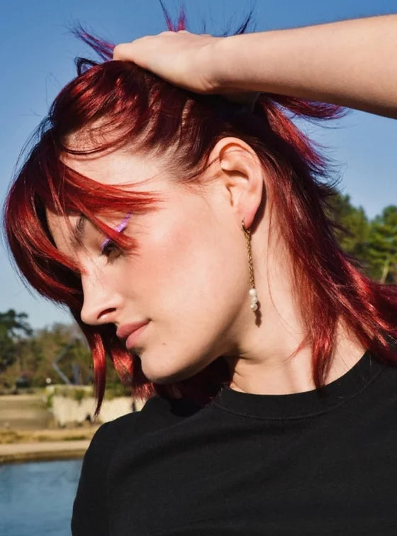 Femme de profil aux cheveux bordeaux - rouges portant une paire de boucles d'oreilles pendantes constitué d'une chaîne et de trois petites perles d'eau douce.