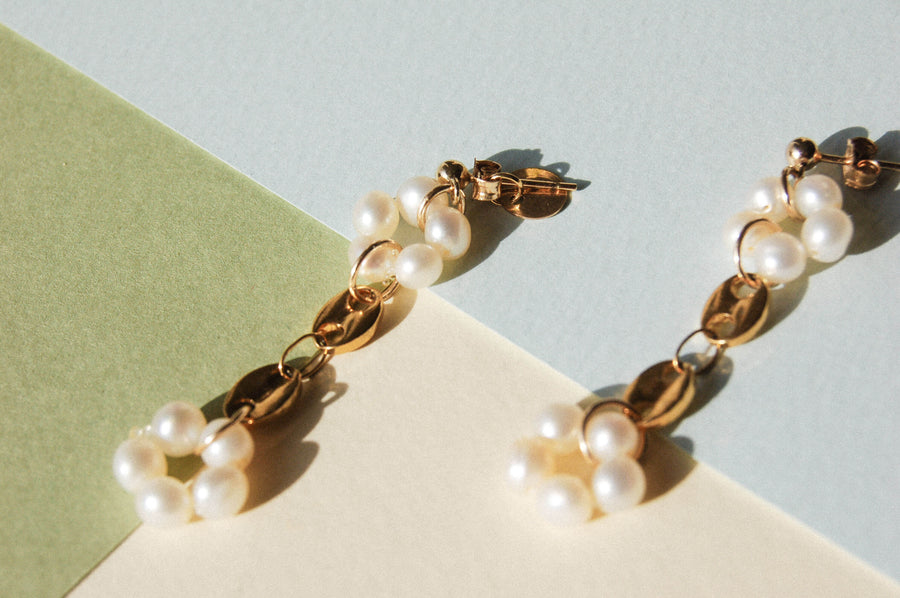 Boucles d'oreilles upcyclées ornées de perles d'eau douce et de grains de café en plaqué or posées sur un fond coloré.. 